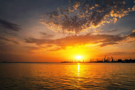 Cranes silhouettes against fiery, orange and red sky. Beautiful Azov Sea at sunrise. Harbor of Berdyansk during sunset.の写真素材