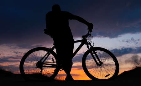 Silhouette of cyclist on the background of sunset. Biker with bicycle on the sand during sunriseの写真素材