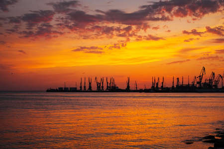 Beautiful landscape with fiery sunset sky and sea. Harbor of Berdyansk during sunrise. Cranes silhouettes against fiery, orange and red sky.の写真素材