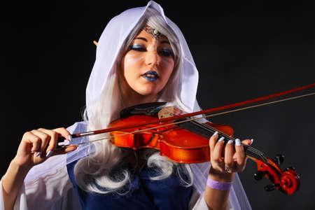 Beautiful girl In an elf costume with a violin on a gray background. Original cosplay characterの写真素材