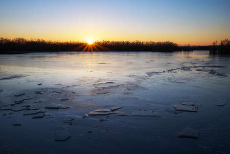 Winter landscape with frozen river, reeds and sunset sky. Daybreakの写真素材