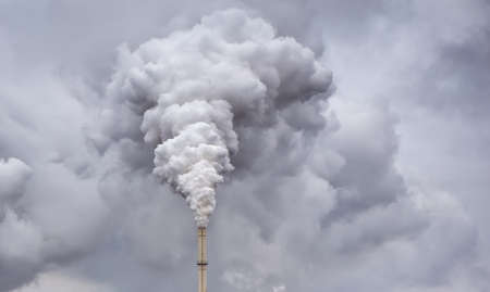 Smoke from factory pipe against dark overcast skyの写真素材