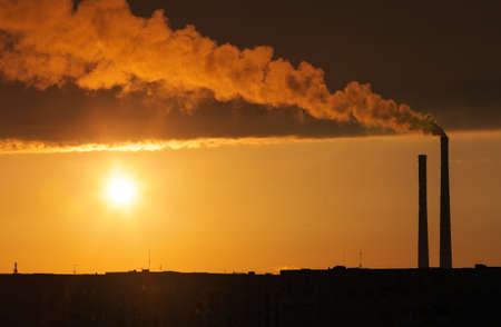 Roofs of city houses during sunset. Dark smoke coming from the thermal power plant pipe.の写真素材