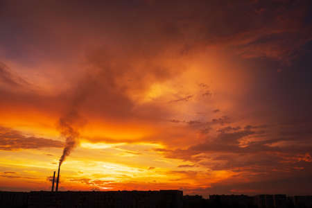 Colorful Magic Sunset. Roofs of city houses during sunrise. Birds flying in the sky. Dark smoke coming from the thermal power plant pipe.の写真素材