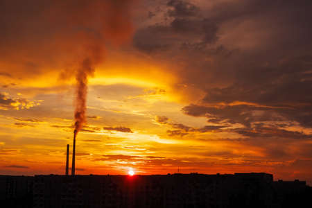 Colorful Magic Sunset. Roofs of city houses during sunrise. Birds flying in the sky. Dark smoke coming from the thermal power plant pipe.の写真素材