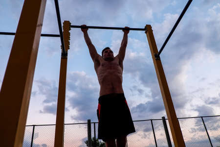 Fitness, sport, exercising, training and lifestyle concept - young man doing pull ups on horizontal...