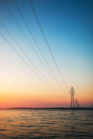 Power lines from the nuclear power plant to the other shore. Beautiful landscape with sunset and a lake.の写真素材