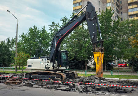 Excavator breaking concrete road surface with hydrohammer drill at repairing roadwork. Overhaul of...