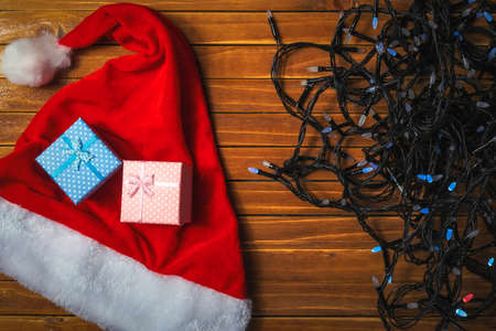 Holiday colorful lights of garland, santa claus hat and gift boxes. Christmas background. Top view.