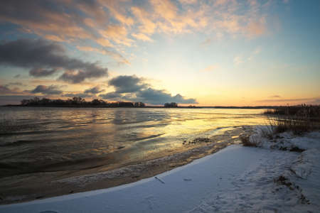Winter landscape with frozen lake and sunset sky. Colorful orange sky. Composition of nature.の写真素材