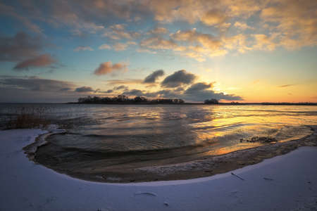 Winter landscape with frozen lake and sunset sky. Colorful orange sky. Composition of nature.の写真素材
