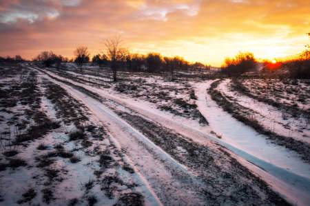 Dirt track through a field of snow at dawn or dusk. A Snow-covered country road through the fields at sunset.の写真素材