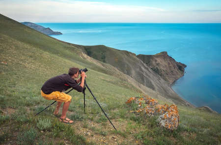 A photographer with a tripod and camera makes photos of landscapes on the mountain. Men in work.の写真素材