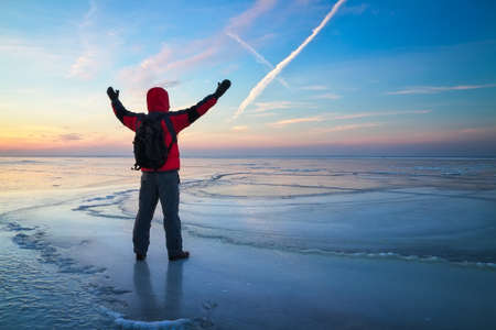 Nature photographer traveler on the frozen lake during sunrise in winter. Beautiful colorful landscape with peopleの写真素材