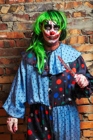 Crazy clown with a knife on a brick wall background. Halloween conceptの写真素材