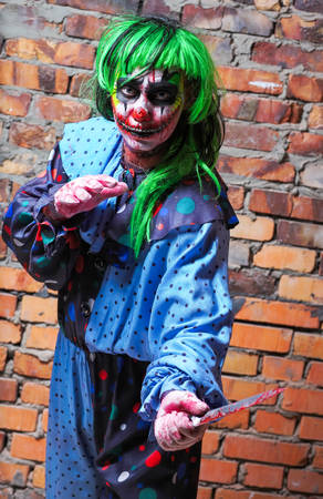 Crazy clown with a knife on a brick wall background. Halloween conceptの写真素材