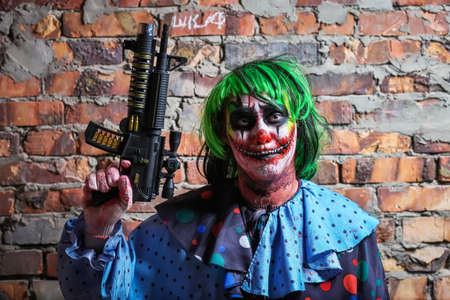Crazy clown with a gun on a brick wall background. Halloween conceptの写真素材
