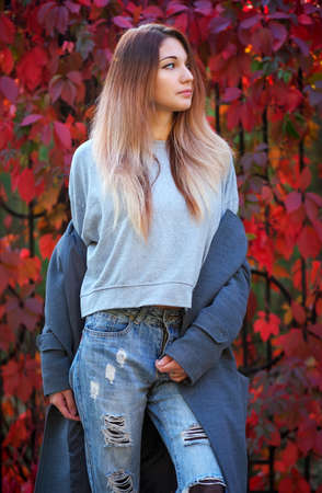 Dreamy beautiful girl with long colorful hair on autumn background of red grape hedge. Inspired woman in gray coat. Autumn euphoria. Female emotional portrait in faded tones.の写真素材