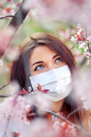 Close up portrait of young girl under a blossoming apricot tree with a mask from the coronavirus.の写真素材