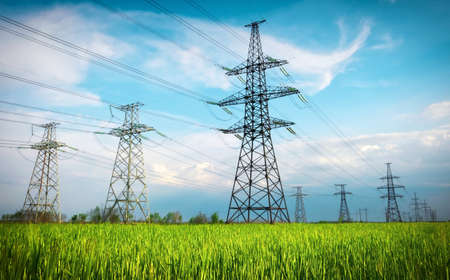 High voltage lines and power pylons in a flat and green agricultural landscape on a sunny day with clouds in the blue sky. Cloudy and rainy. Wheat is growingの写真素材