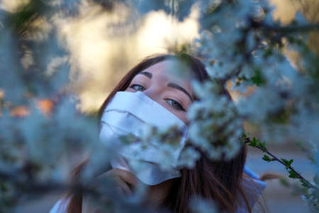 Close up portrait of young girl under a blossoming tree with a mask from the coronavirus.