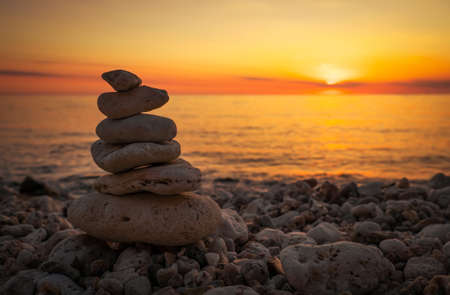 Pyramid of the small pebbles on the beach. Stones, against the background of the sea shore during sunsetの写真素材