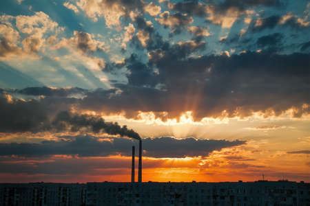 Colorful Magic Sunset. Roofs of city houses during sunrise. Dark smoke coming from the thermal power plant pipe.の写真素材