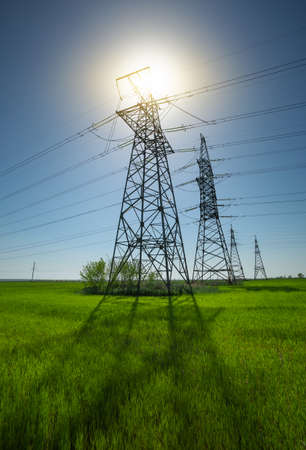 High voltage lines and power pylons in a flat and green agricultural landscape on a sunny day with clouds in the blue sky.の写真素材