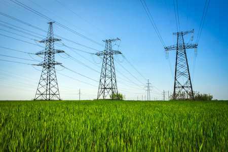 High voltage lines and power pylons in a flat and green agricultural landscape on a sunny day with clouds in the blue sky.の写真素材