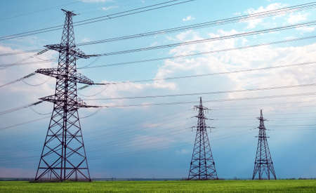 High voltage lines and power pylons in a flat and green agricultural landscape on a sunny day with clouds in the blue sky. Cloudy and rainy. Wheat is growingの写真素材