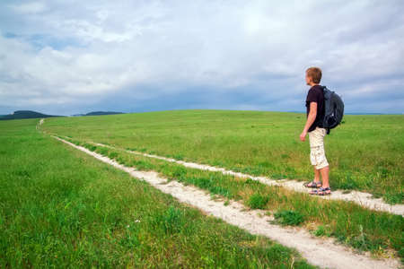 Male traveler is walking through the field on the background of the mountainsの写真素材