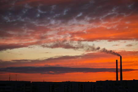 Colorful Magic Sunset. Roofs of city houses during sunrise. Dark smoke coming from the thermal power plant pipe.の写真素材