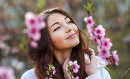 Smiling beautiful girl standing near a peach tree during sunset. Happy face. Spring time.の写真素材