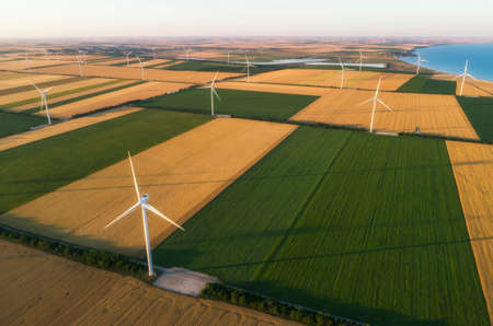 Aerial view of renewable windmills turbines supplying cultivation area with eco power getting energy from wind blowing on vast area of agriculture meadows next to sea. Alternative electricityの写真素材