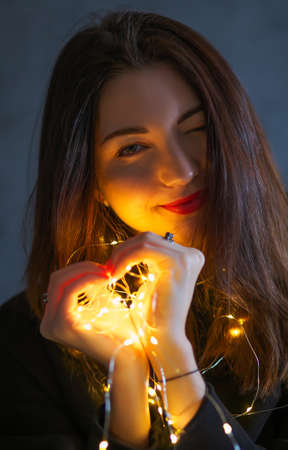 A girl with a Christmas garland. Light in hands, in the form of a heartの写真素材