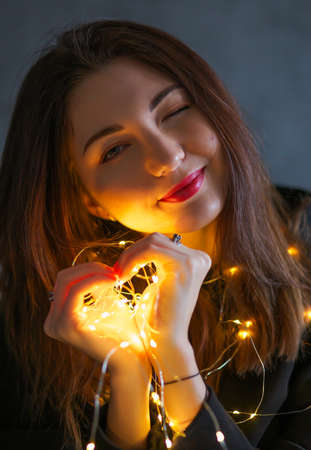 A girl with a Christmas garland. Light in hands, in the form of a heartの写真素材