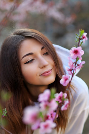Smiling beautiful girl standing near a peach tree during sunset. happy face. springtime.の写真素材