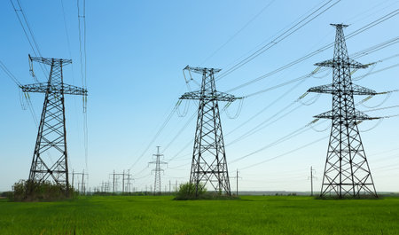 High voltage lines and power pylons in a flat and green agricultural landscape on a sunny day with clouds in the blue sky. Cloudy and rainy. Wheat is growingの写真素材