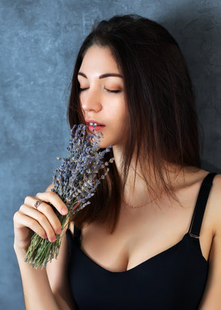 Beautiful girl posing in the studio on a dark background. She holds a small bouquet of lavender in her hands. close-up portrait.の写真素材