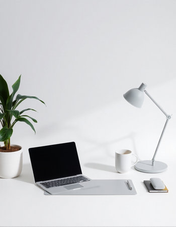 Minimalistic workplace with laptop, coffee cup, notebook and houseplant on white background.