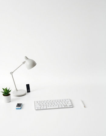 White office desk with keyboard, mouse, pen, smartphone and plant.
