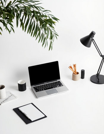 Modern workspace with laptop, coffee cup, stationery and palm leaf on white background