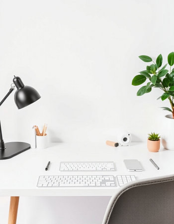 Minimal workspace with computer, keyboard, stationery and plant on white wall backgroundの写真素材