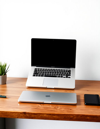 Laptop with blank screen on wooden table and white wall background.