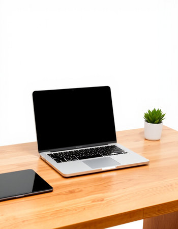 Laptop with blank screen on wooden table and white wall background.
