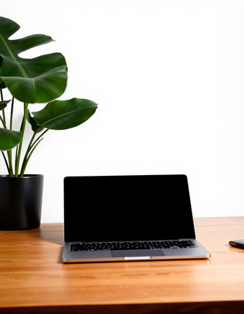 Laptop with blank screen on wooden table and green plant on white background