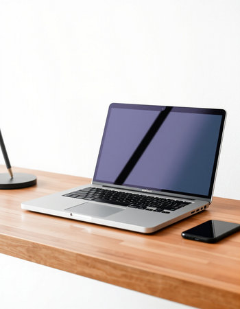 Laptop with blank screen on a wooden table against a white wall