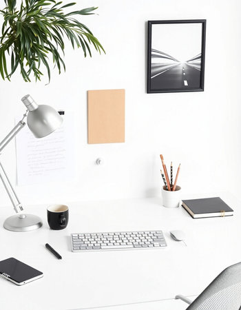 White office desk with laptop, coffee cup, notebook and picture frame on the wallの写真素材