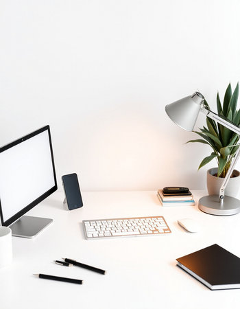 White office desk with computer, smartphone, stationery and plant.