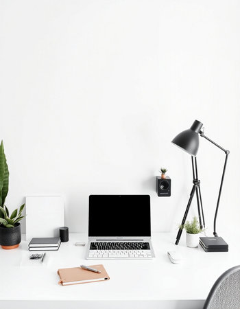 Workplace with laptop, lamp and stationery on table near white wall